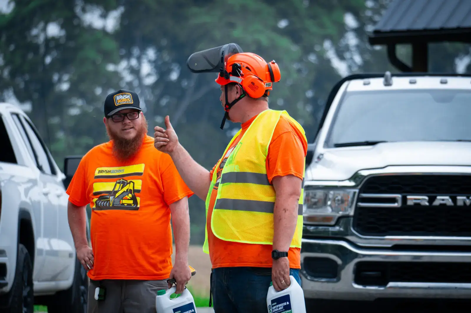 Two crew members in Brushworks shirts on a job site, one giving a thumbs up