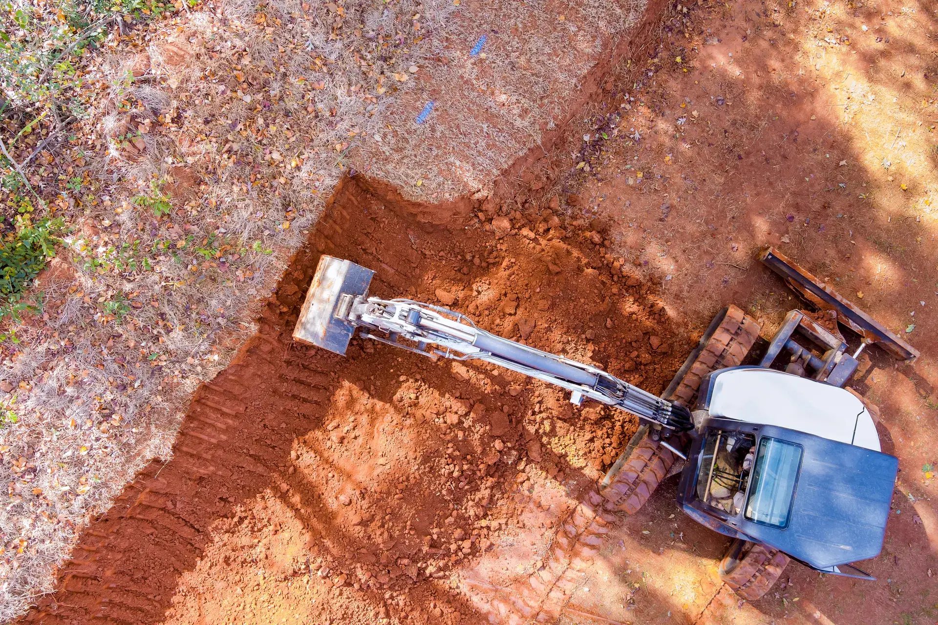Overhead view of a mini excavator digging a trench in red clay