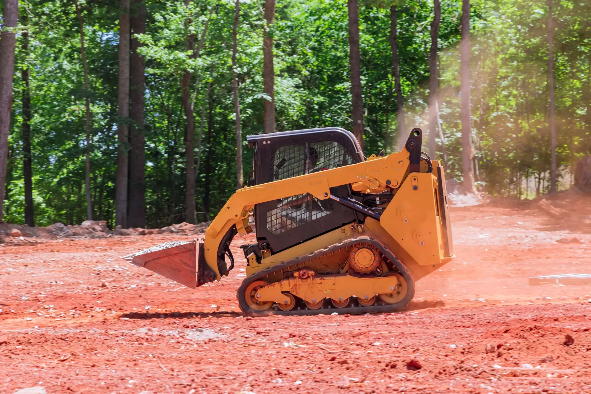 Track loader working cleared red-clay ground at the edge of the woods